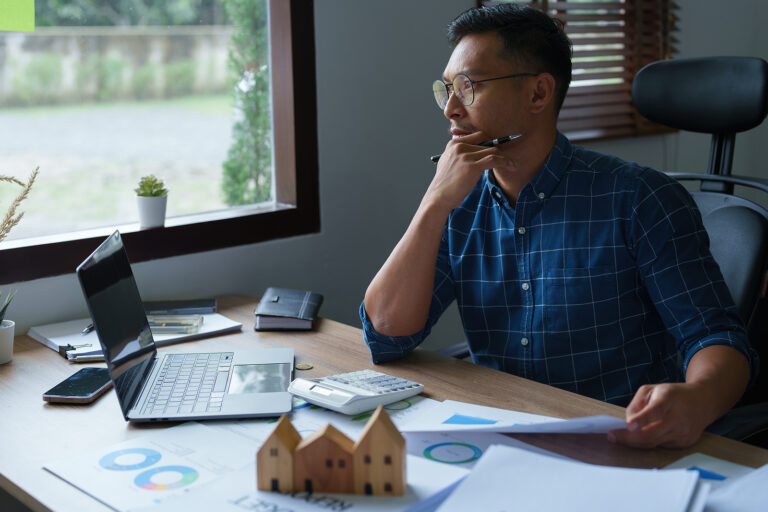 A young man using a calculator to calculate his home budget to assess the risks of investing in real estate and using personal credit for business expenses