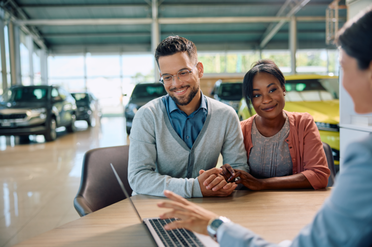 Young couple and car saleswoman using laptop in a showroom asking how to minimize impact of rate shopping on your fico scores.